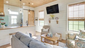 A spacious living room with a grey sofa, a wooden coffee table, and a television mounted on the wall. - Contrell Cottage On Farm w/ Peaceful Views (Lena)