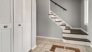 A staircase with wooden steps and a black handrail, leading to a landing with a white door and a window.