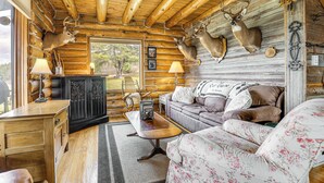 Ein Holzhaus-Interieur mit Holzbalkendecke, montierten Hirschköpfen, einer Couch, einem Tisch und einem Schrank.