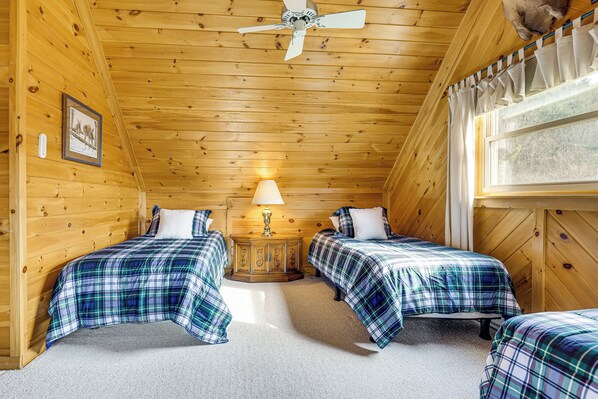 Une cabine équipée de deux lits, d’un ventilateur de plafond, d’une fenêtre avec des rideaux et d’une lampe posée sur une table de chevet en bois.