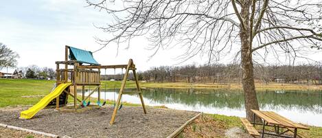 A playground with a slide and swings near a lake.