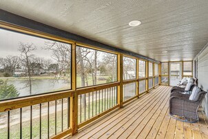 Un porche cubierto con barandillas de madera, un sofá de mimbre y vistas a un lago y árboles.