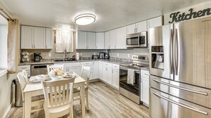 Una cocina moderna con armarios blancos, electrodomésticos de acero inoxidable y un comedor con mesa y sillas.