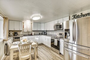 Una cocina moderna con armarios blancos, electrodomésticos de acero inoxidable y un comedor con mesa y sillas.