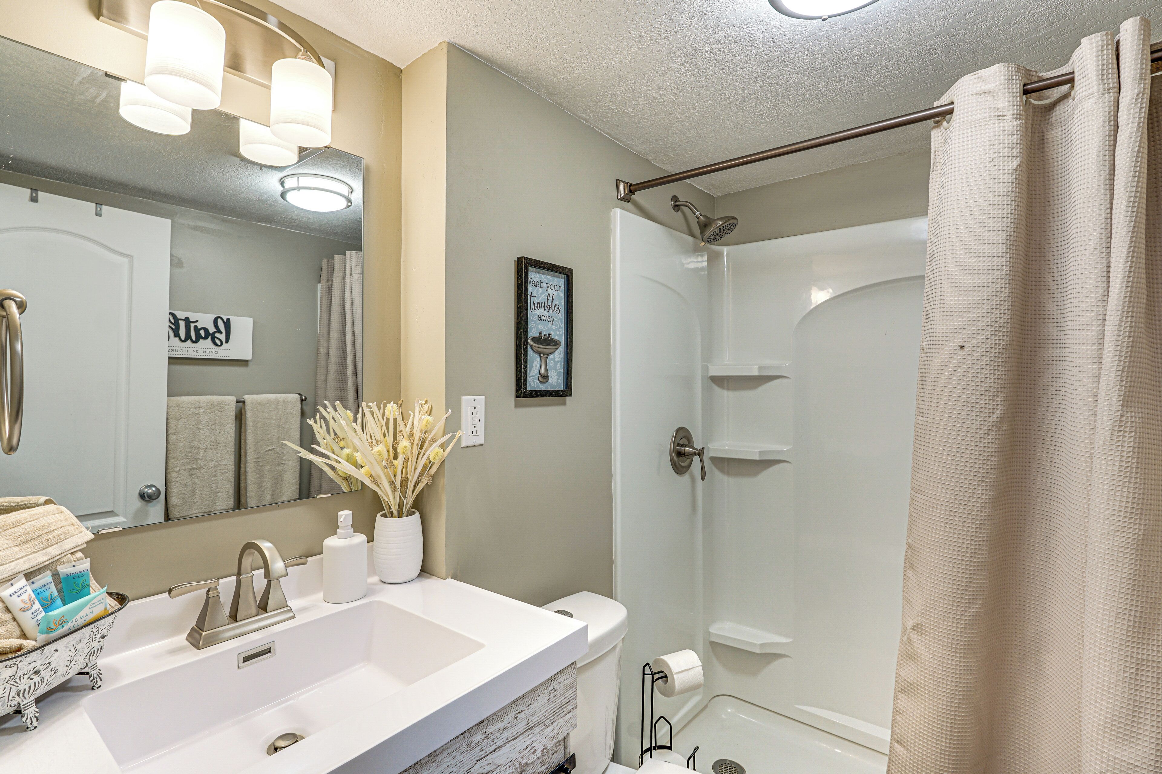 Une salle de bain avec un lavabo blanc, un miroir et une douche. On y trouve des serviettes et des articles de toilette sur le lavabo.