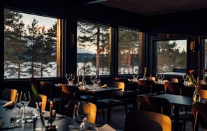 A restaurant with tables set for dining, large windows with a view of trees and snow, and a warm interior lighting. - Kelo Resort (Enontekio)
