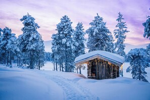 A log cabin with a snow-covered roof, surrounded by snow-laden trees, and a clear sky. - Kelo Resort (Enontekio)