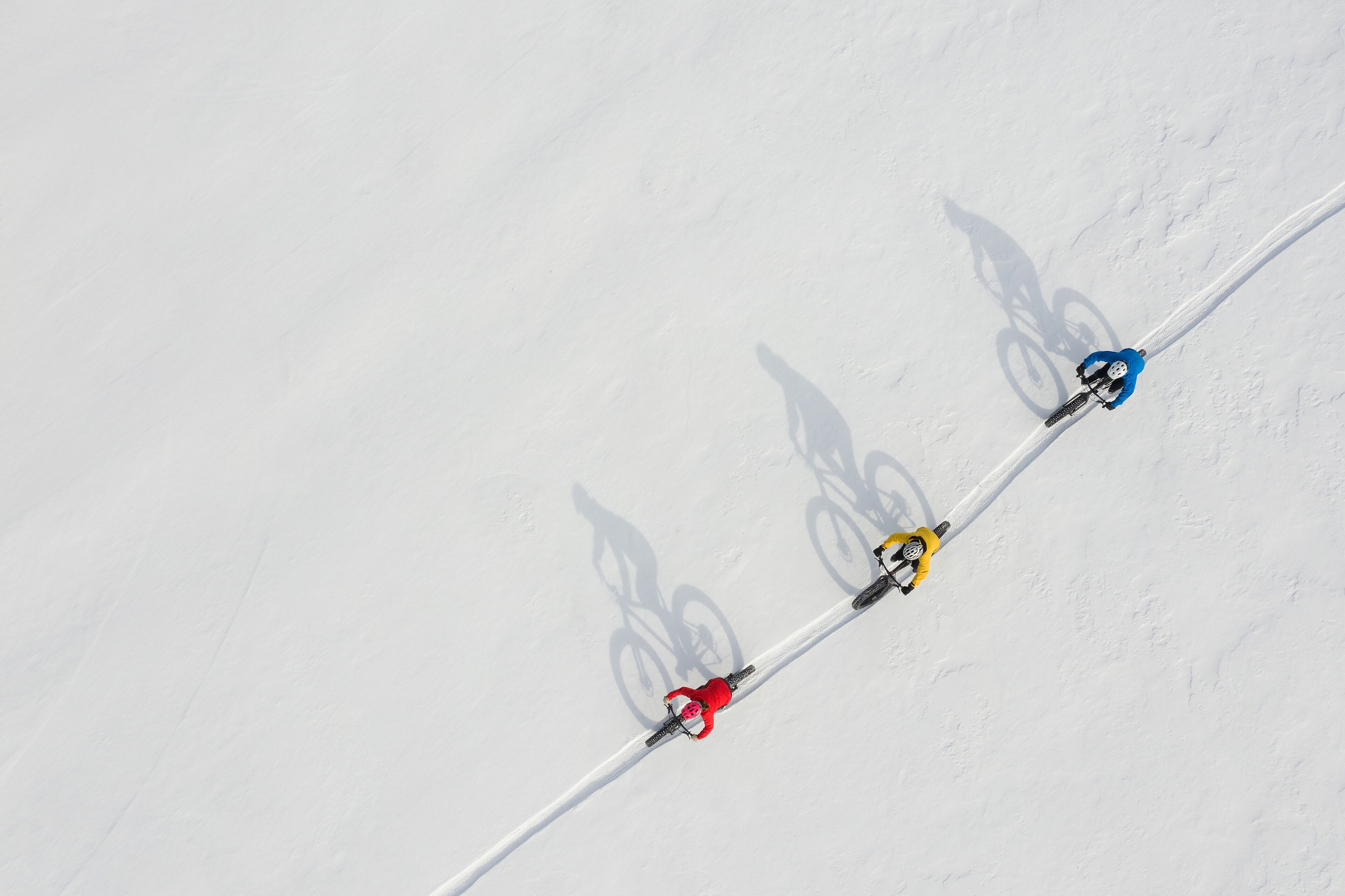 A ski slope with three skiers in red, yellow, and blue jackets.