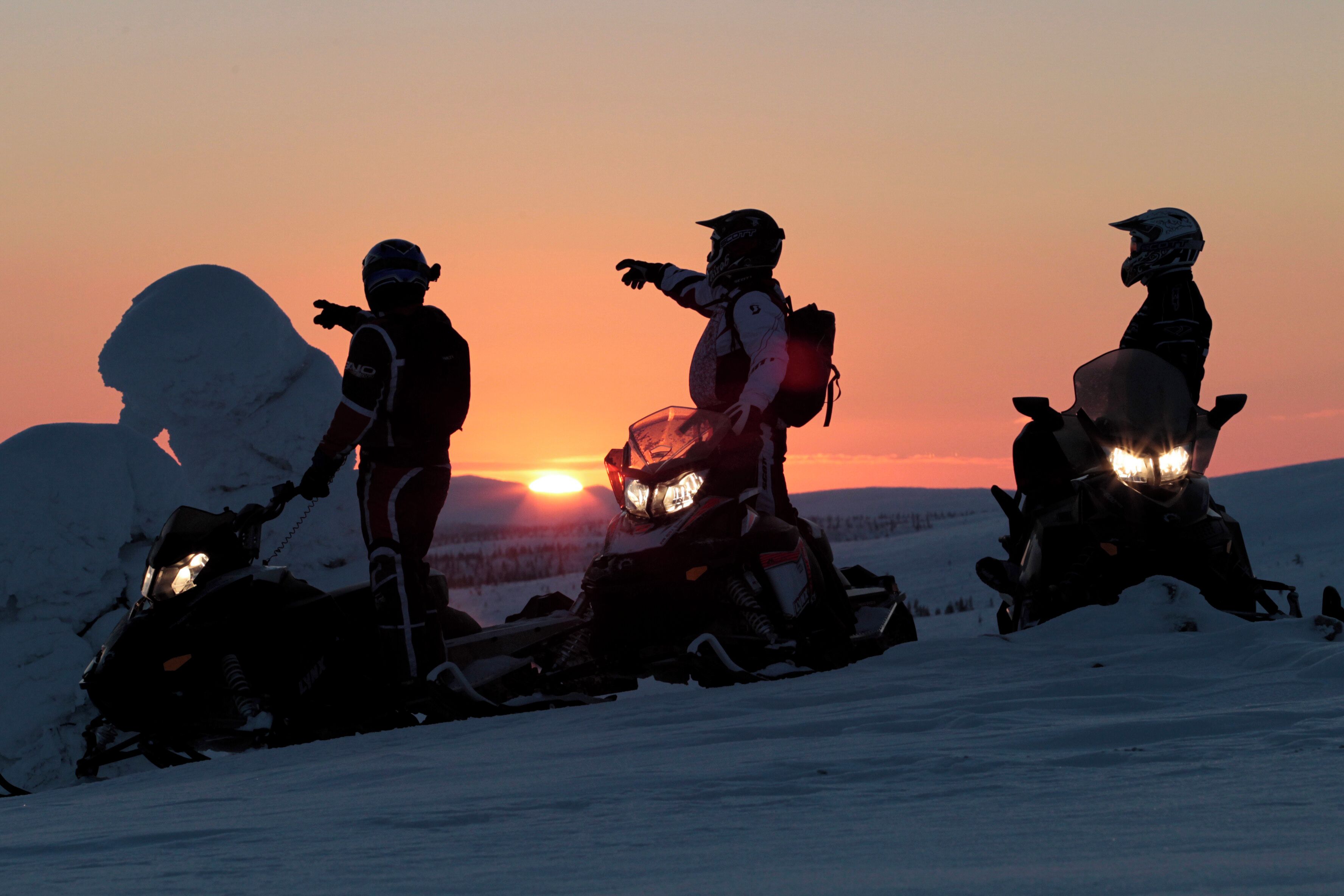 Trois motoneiges sur un paysage enneigé au coucher du soleil.