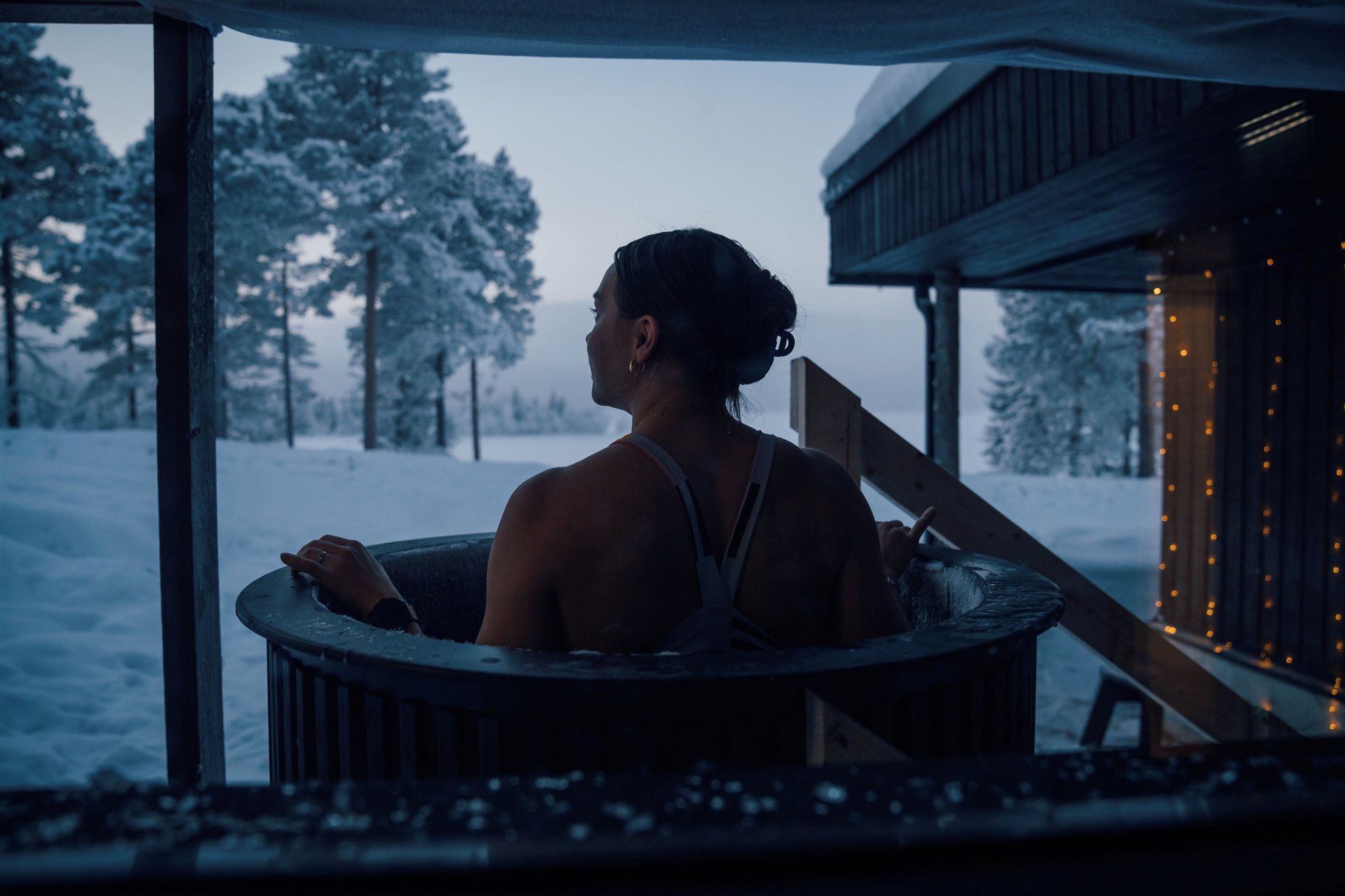 Una persona en un jacuzzi con un paisaje nevado visible a través de la ventana.