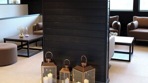 Un intérieur moderne avec un mur noir sur lequel est inscrit le texte « KELO RESORT ». On y voit trois lanternes en verre contenant des bougies, posées sur le sol.