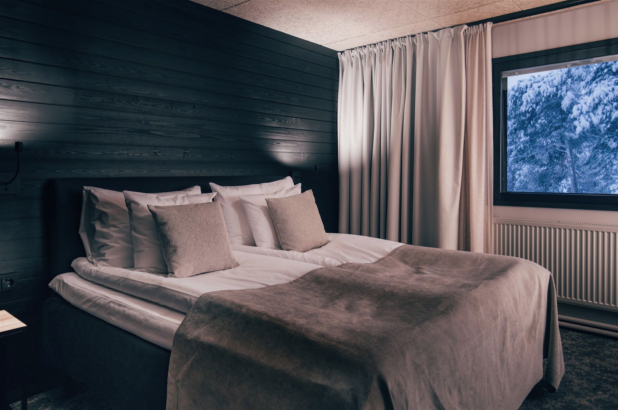 Une chambre à coucher avec un lit, des oreillers, une fenêtre avec des rideaux et une vue sur les arbres.