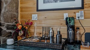 A wooden wall with a framed black and white photograph, a coffee machine, a glass carafe, a cocktail shaker, a bottle, and a small white device on a tray. - Screened-Porch Home, Killington Views & Pet-Friendly (Hartford)