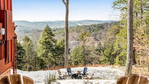 A view from a cabin with a snow-covered ground, wooden chairs, and a forested landscape. - Screened-Porch Home, Killington Views & Pet-Friendly (Hartford)