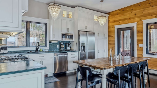 A modern kitchen with white cabinets, stainless steel appliances, a wooden dining table, and black chairs. - Screened-Porch Home, Killington Views & Pet-Friendly (Hartford)