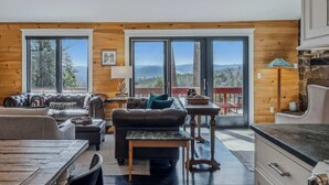 A cozy living room with leather sofas, a coffee table, and a view of the mountains through large windows. - Screened-Porch Home, Killington Views & Pet-Friendly (Hartford)