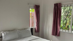 A modern hotel room with a large bed, a window with curtains, and a view of greenery outside. - Spacious 2bdr BangTao House  (Choeng Thale)