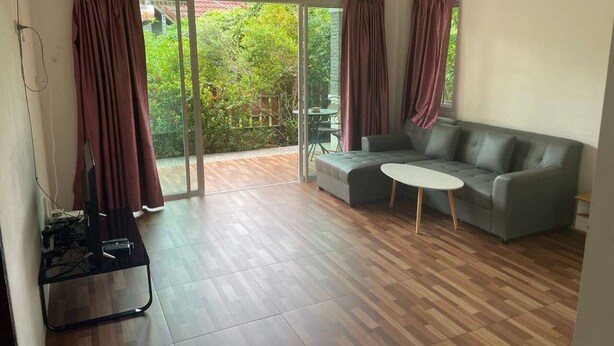 A spacious living room with a grey sofa, a small round table, and a TV on a stand. - Spacious 2bdr BangTao House  (Choeng Thale)