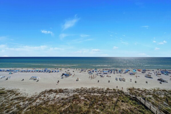 A beach with umbrellas and sun loungers, a sandy shore, and a clear blue sky.