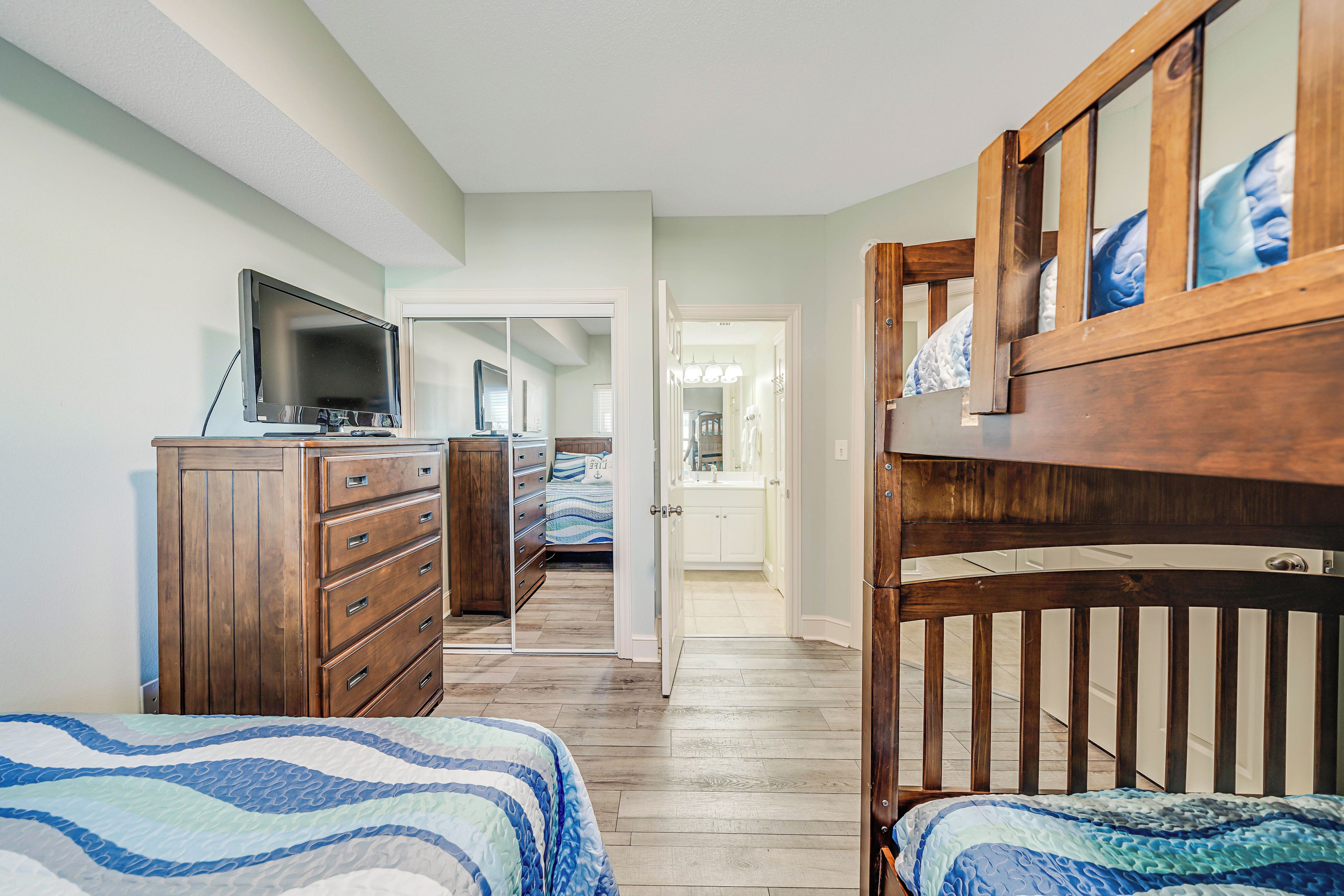 A bedroom with two beds, a dresser, a television, and a wooden crib.