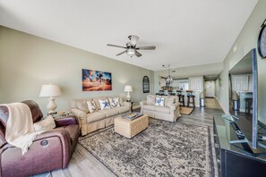 A living room with two sofas, a coffee table, a TV, and a ceiling fan. - Majestic Tower 2-508 Beachfront, Pools, Hot Tubs, Gym, Tennis, FREE Perks! (Panama City Beach)