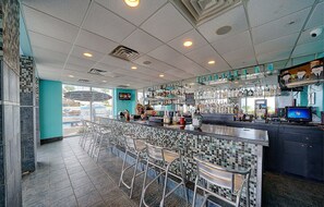 A bar area with a tiled floor, metal chairs, and a counter with various bottles. - Majestic Tower 2-508 Beachfront, Pools, Hot Tubs, Gym, Tennis, FREE Perks! (Panama City Beach)