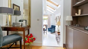 Un salon moderne avec un fauteuil bleu, une table basse en bois et une lampe. On y trouve un bureau avec un ordinateur et un vase rempli de fleurs rouges.