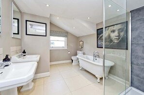 Un baño moderno con dos lavamanos, una bañera independiente, inodoro y cabina de ducha.