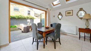 Un coin repas avec une table en bois et des chaises à revêtement gris, un radiateur et une fenêtre donnant sur un jardin.