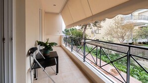 A balcony with a table and chairs, a potted plant, and a view of a garden and buildings. - Seaside Astros Getaway - La Maison Etoile (North Kynouria)