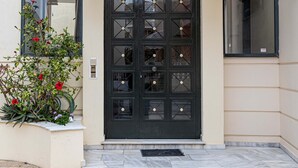 A modern building entrance with a black door, a glass balcony, and a small garden with red flowers. - Seaside Astros Getaway - La Maison Etoile (North Kynouria)