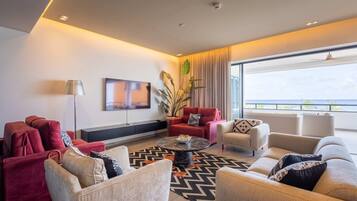 A modern living room with a large window, red and beige sofas, a coffee table, and a flat-screen TV mounted on the wall.