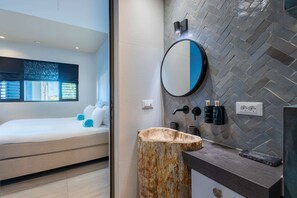 Une salle de bain moderne avec un miroir rond, un lavabo en bois et un mur orné d’un motif en chevrons.