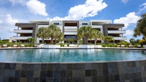 Un hotel moderno con piscina, varios balcones y palmeras.