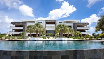 Um hotel moderno com piscina, várias varandas e palmeiras.