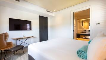 Quarto de hotel moderno com uma cama grande, uma escrivaninha, uma cadeira e uma televisão na parede.