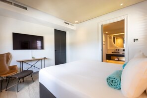 Une chambre d’hôtel moderne, dotée d’un grand lit, d’un bureau, d’une chaise et d’un téléviseur fixé au mur.