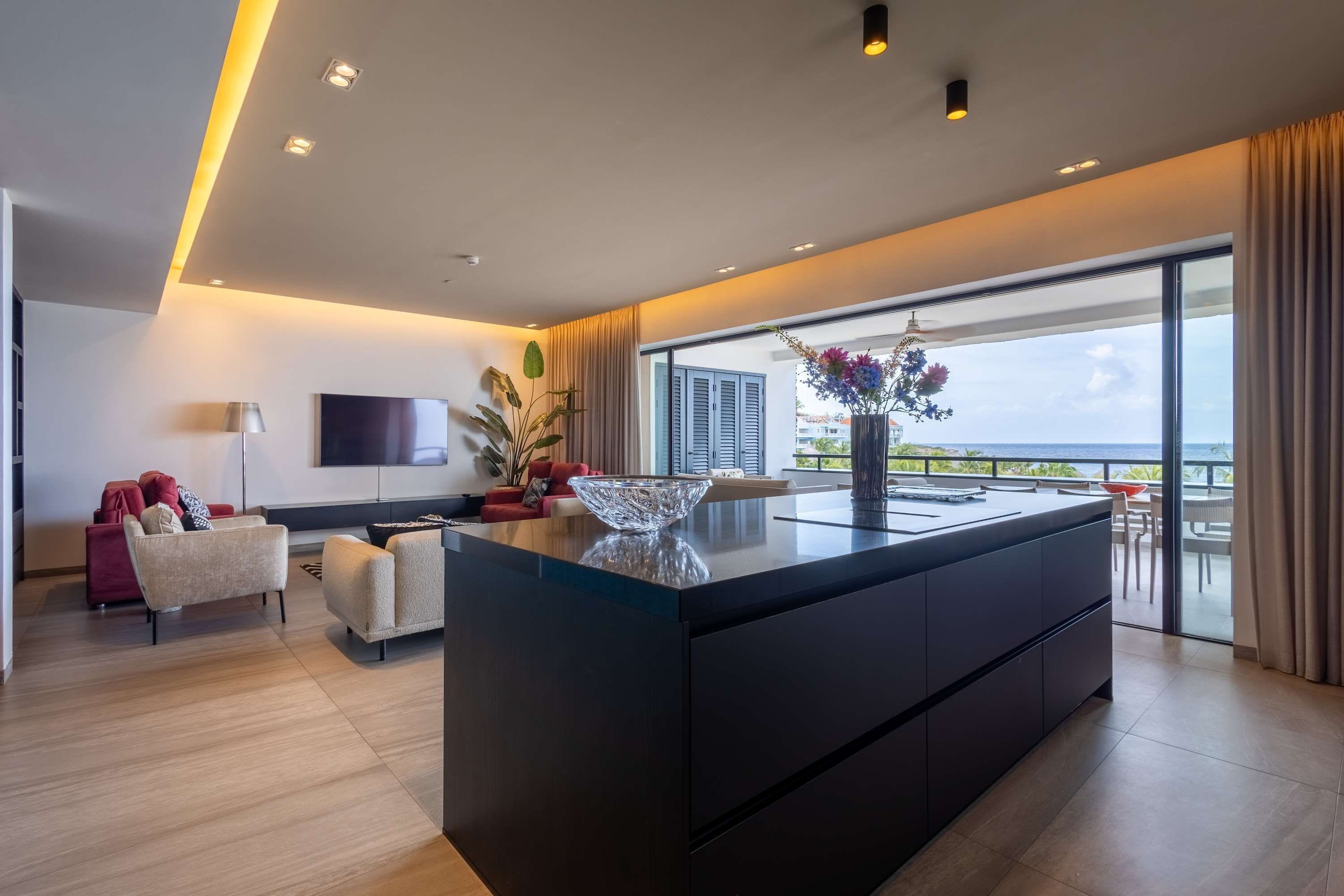Cozinha moderna com uma ilha grande, televisão de tela plana e vista para o mar através de amplas janelas.