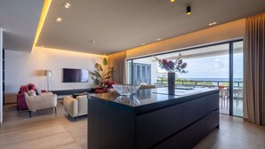 Una cocina moderna con una isla grande, un televisor de pantalla plana y vistas al mar a través de ventanas amplias.