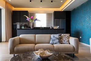 A modern living room with a beige sofa, a marble coffee table, and a kitchen in the background.
