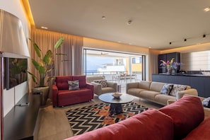 Un salon moderne avec un canapé rouge, un canapé beige et une table basse. Une grande fenêtre offre une vue sur la ville.