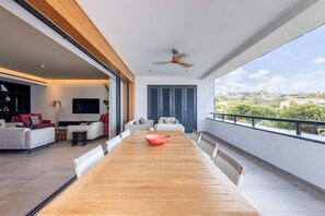 Un balcon spacieux avec un coin repas comprenant une table et des chaises en bois, un centre de table composé d’un bol rouge, et une vue sur un quartier résidentiel.