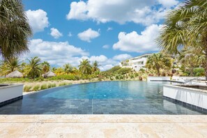 Une piscine d’un bleu éclatant, entourée de palmiers, avec un bâtiment blanc en arrière-plan.