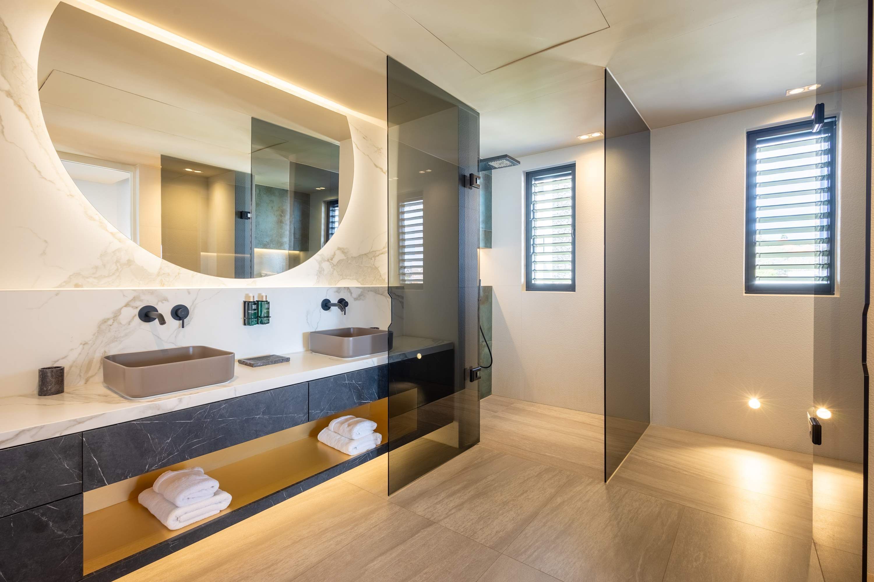 Un baño moderno con tocador de mármol, un espejo grande y cabina de ducha de vidrio.