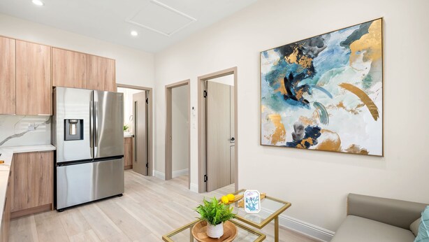 A modern kitchen with stainless steel appliances, wooden cabinets, and a glass coffee table with a plant.