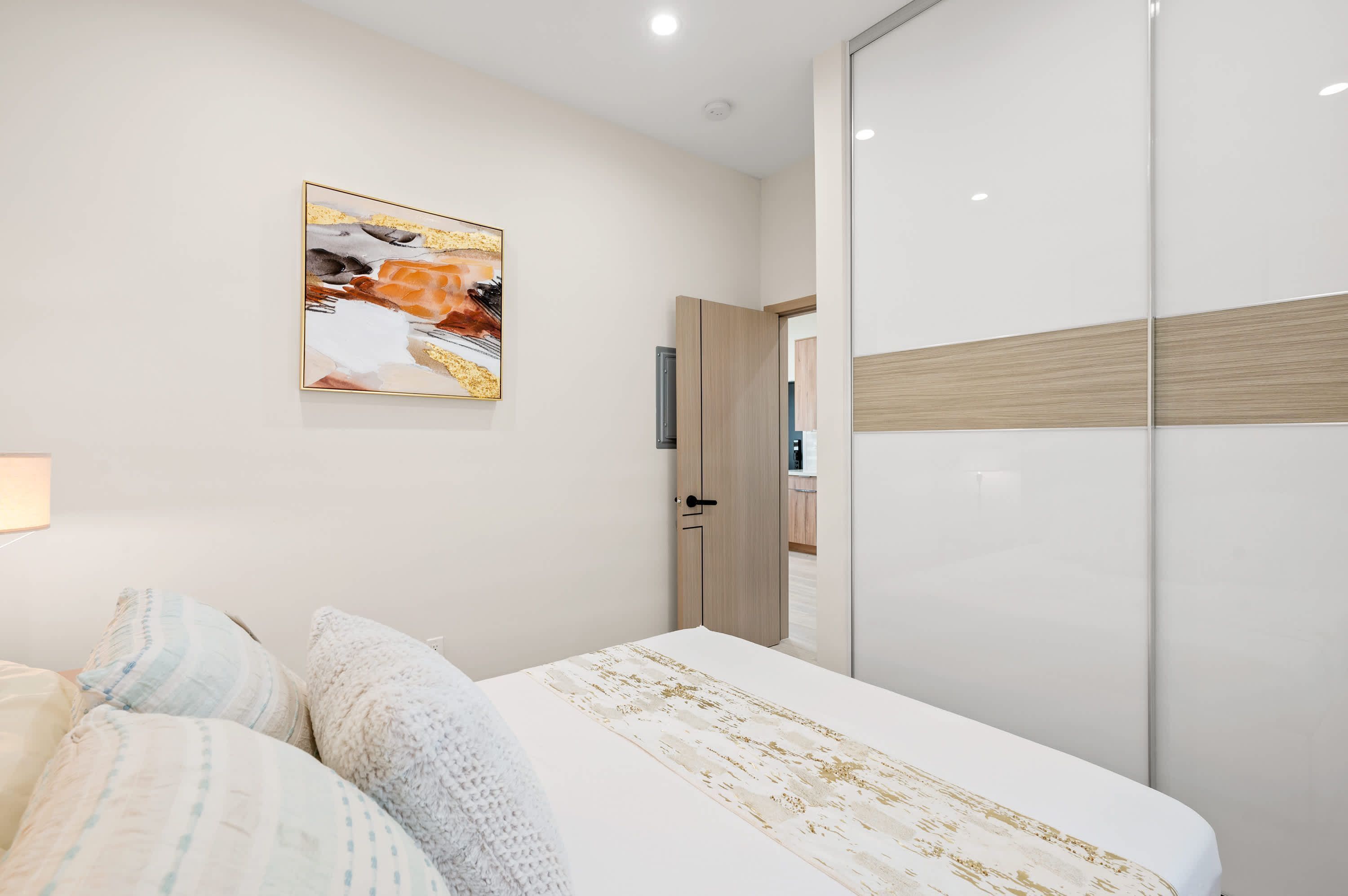 Une chambre à coucher avec un lit, une armoire, un tableau au mur et une porte donnant sur une autre pièce.