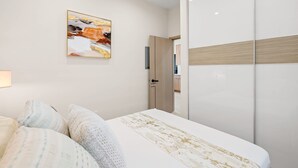 A bedroom with a bed, a wardrobe, a painting on the wall, and a door leading to another room.