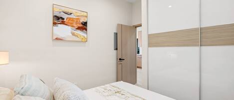 Une chambre à coucher avec un lit, une armoire, un tableau au mur et une porte donnant sur une autre pièce.