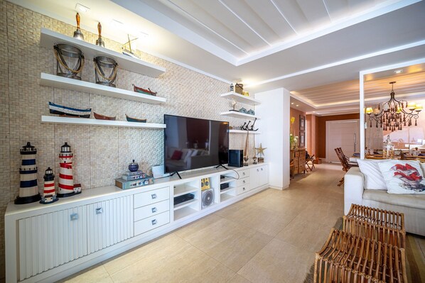 Una sala de estar moderna con un televisor de pantalla plana grande, muebles blancos y elementos decorativos como faros y una araña.