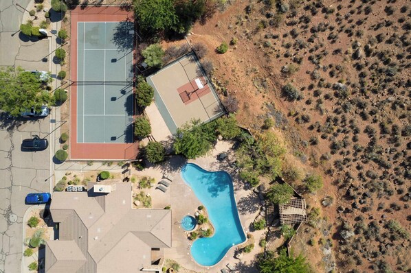 An aerial view of a residential property with a swimming pool, tennis court, and a fenced garden area.